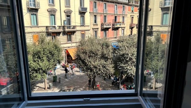 Blick durch ein Fenster auf eine Straße mit Gebäuden, Bäumen und abgestellten Fahrzeugen.