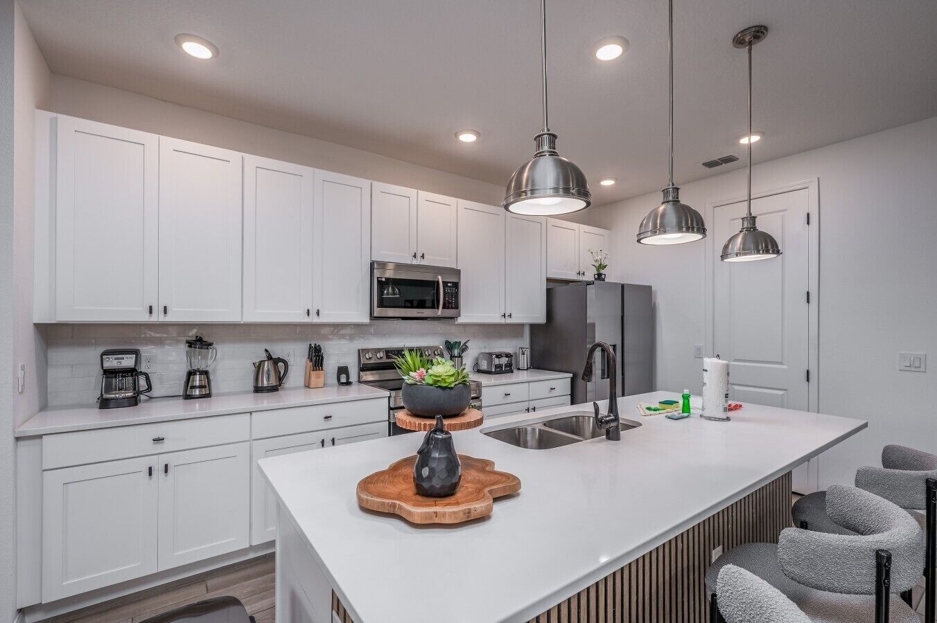 Una cocina moderna con armarios blancos, electrodomésticos de acero inoxidable e iluminación colgante.