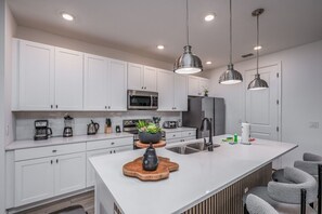 A modern kitchen with white cabinetry, stainless steel appliances, and pendant lighting. - New Construction - Cozy Home & Playroom (Davenport)