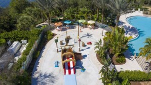 An aerial view of a resort with a swimming pool, palm trees, and outdoor seating areas. - New Build - Cozy House & Game Room (Davenport)