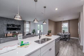 A modern kitchen with a central island, pendant lighting, and a dining area with a table and chairs. - New Construction - Cozy Home & Playroom (Davenport)