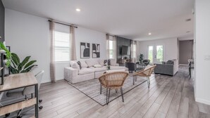 A modern living room with a sectional sofa, two armchairs, a coffee table, and a TV mounted on the wall. - New Build - Cozy House & Game Room (Davenport)