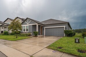 A residential house with a garage, a driveway, and a well-maintained lawn. - New Construction - Cozy Home & Playroom (Davenport)