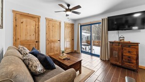 Ein Wohnzimmer mit Sofa, Couchtisch, Holztüren, Deckenventilator und einem an der Wand befestigten Fernseher.