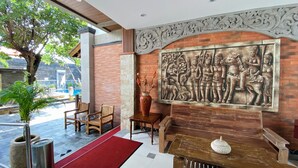 A reception area with a mural, wooden furniture, and a red carpet. - Pepitu Dormitory By Sandat (Legian)