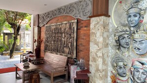A room with a large mural, a wooden bench, and a table with a vase. - Pepitu Dormitory By Sandat (Legian)