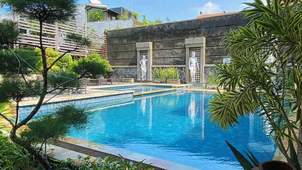A swimming pool with stone tiles, surrounded by greenery and a stone wall. - Pepitu Dormitory By Sandat (Legian)