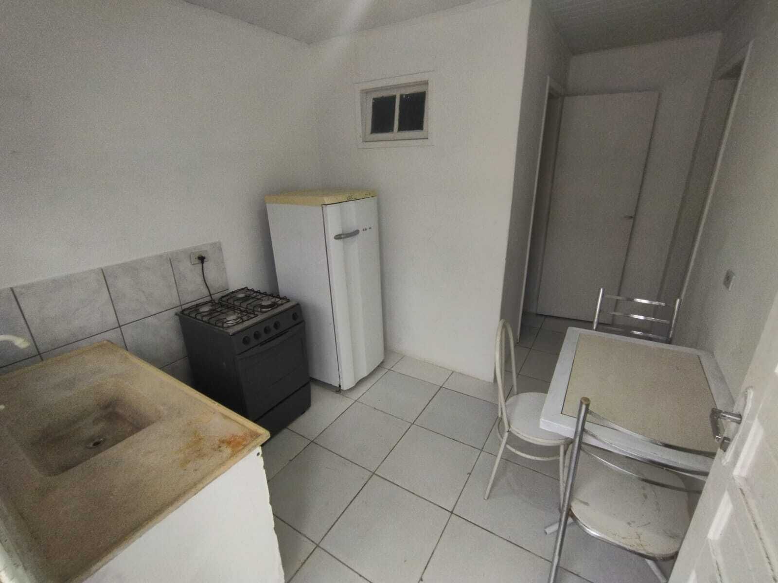 A small, compact kitchen with a gas stove, a white refrigerator, a small sink, and a white chair.