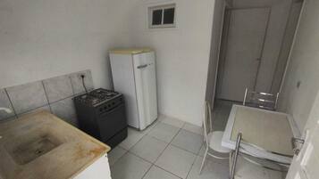 A small, compact kitchen with a gas stove, a white refrigerator, a small sink, and a white chair.