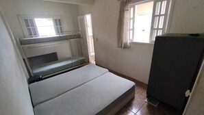 A small, single-room dormitory with a bunk bed, a window with curtains, and a refrigerator. - Pousada da Pedra do Mar (Matinhos)