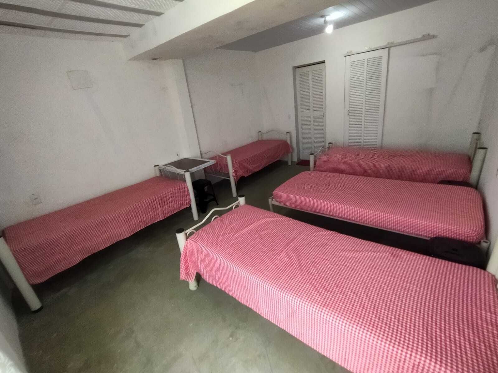 A dormitory room with four single beds, a small table, and a chair.