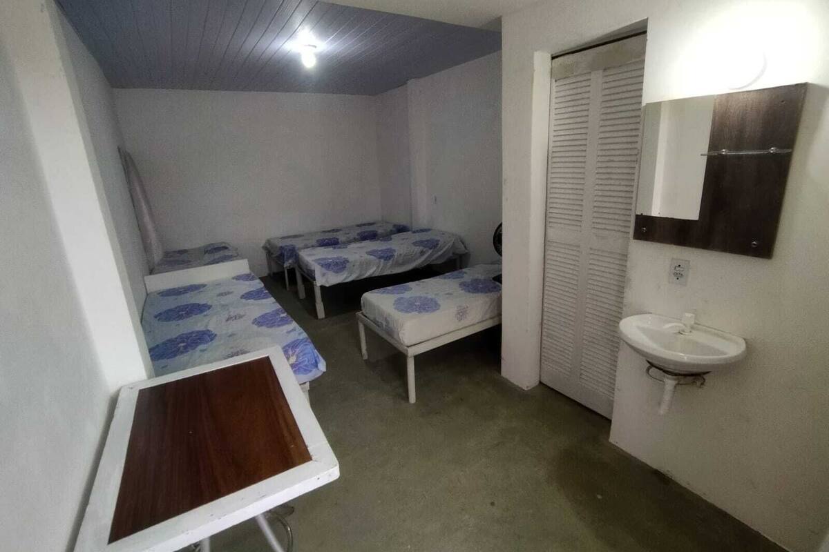 Une petite chambre, de taille modeste, comprenant deux lits simples, une table de chevet, un miroir et un lavabo.