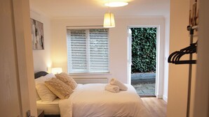 Un dormitorio con cama, ventana con persianas, lámpara colgante y vista a la vegetación exterior.