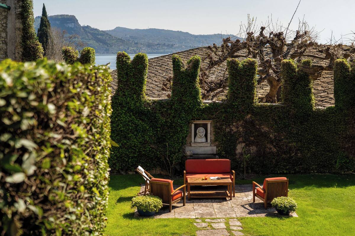 A garden with a stone bench, two chairs, and a statue.