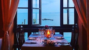 Mesa para dos con una vela, frente a un amplio ventanal arqueado con vista al mar.