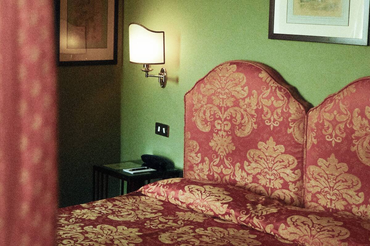A hotel room with a bed, a nightstand, a lamp, and framed pictures on the wall.