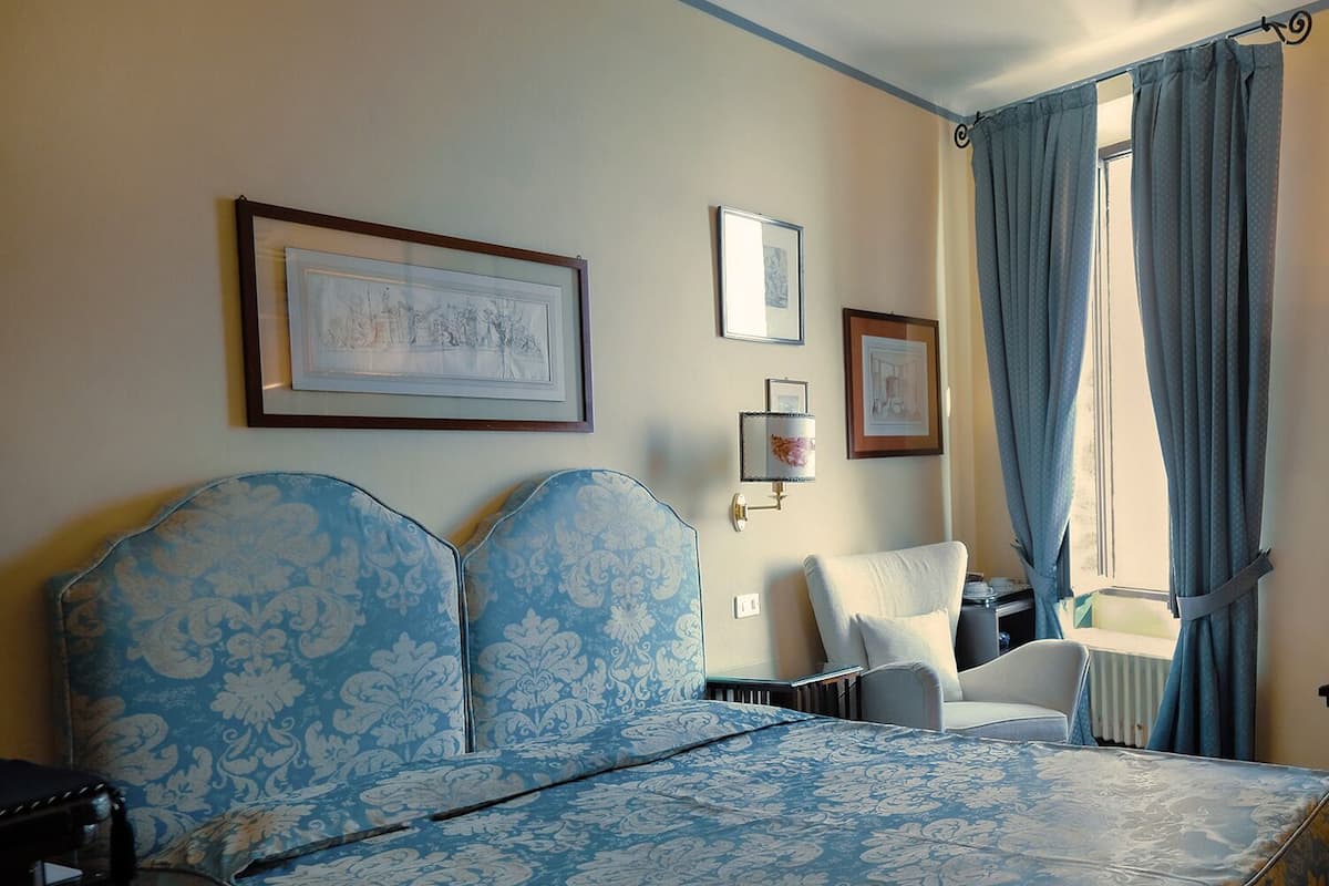 A bedroom with a large bed, a chair, a radiator, and a window with curtains.
