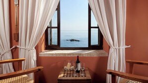 Una habitación con ventana que da al mar, una mesa de madera con una botella y vasos, y dos sillas.