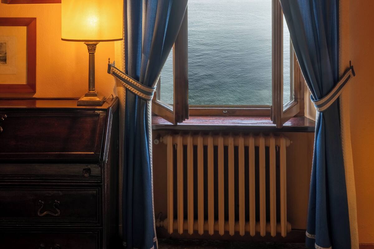 A room with a view of the sea through curtains, a lamp, and a radiator.