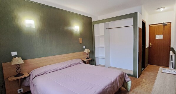 A bedroom with a wooden bed, two bedside lamps, a wall-mounted light, and a door with a handle. - Scopa Rossa (Evisa)