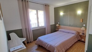Una camera da letto con un letto, una sedia, una finestra con tende e due abat-jour.