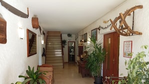 Un corridoio con una scala in legno, piante in vaso e arredamento rustico, tra cui una sega e un corno di cervo in legno.