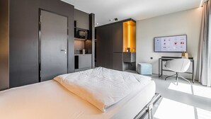 Une chambre d’hôtel moderne équipée d’un lit, d’un bureau, d’une chaise et d’un téléviseur fixé au mur.