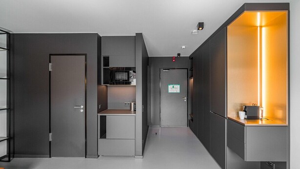 Un couloir moderne avec un coin cuisine, un grand miroir et un luminaire lumineux.