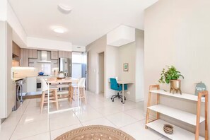 A modern kitchen with stainless steel appliances, a dining area with a wooden table and chairs, and a small office space with a desk and chair.