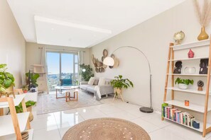 Een moderne woonkamer met een bank, salontafel en vloerlamp. Er is een boekenkast met boeken en decoratieve objecten.