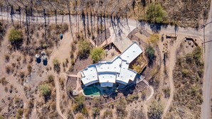 Une vue aérienne d’un bâtiment moderne à l’architecture originale, doté d’un toit incurvé, et entouré d’un espace paysager agrémenté de sentiers et d’une végétation clairsemée.