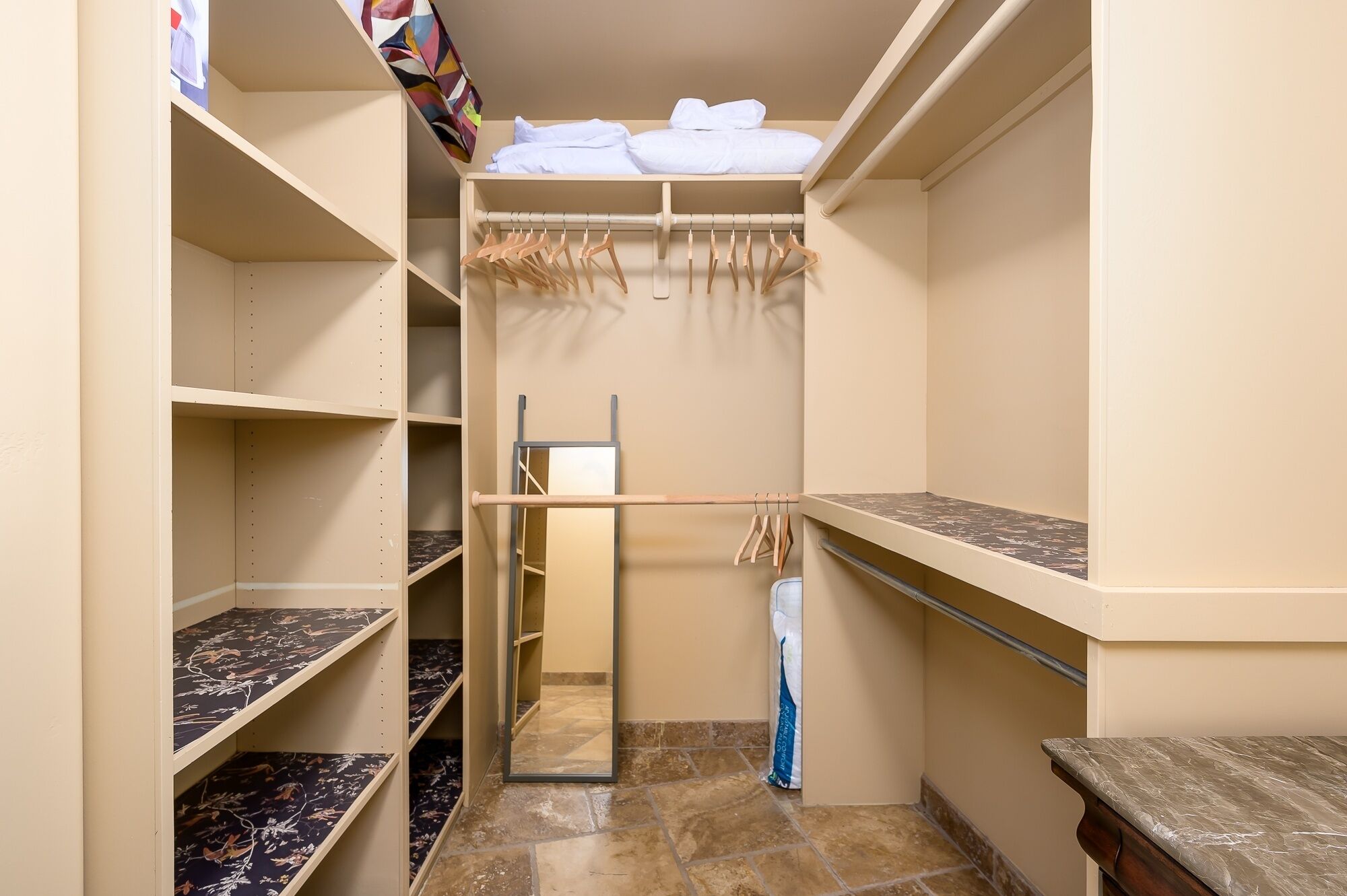 A walk-in closet with open shelves, a hanging rod, and a small table.