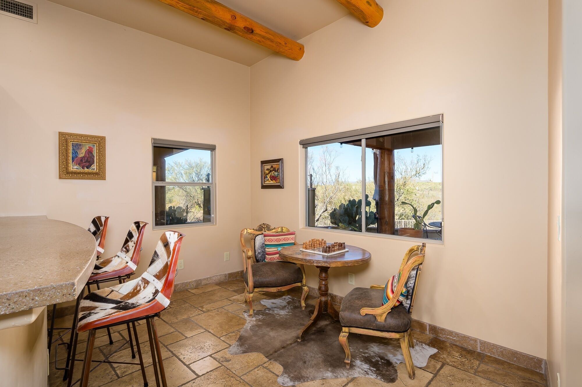 A dining area with a round table, two chairs, and a window with a view of a desert landscape.