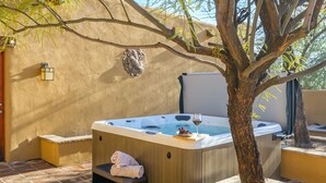 Un bain à remous avec une serviette et des chaussons, un arbre et un luminaire fixé au mur.