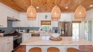 Une cuisine moderne avec des meubles blancs, un grand îlot central doté de tabourets et un réfrigérateur en acier inoxydable.