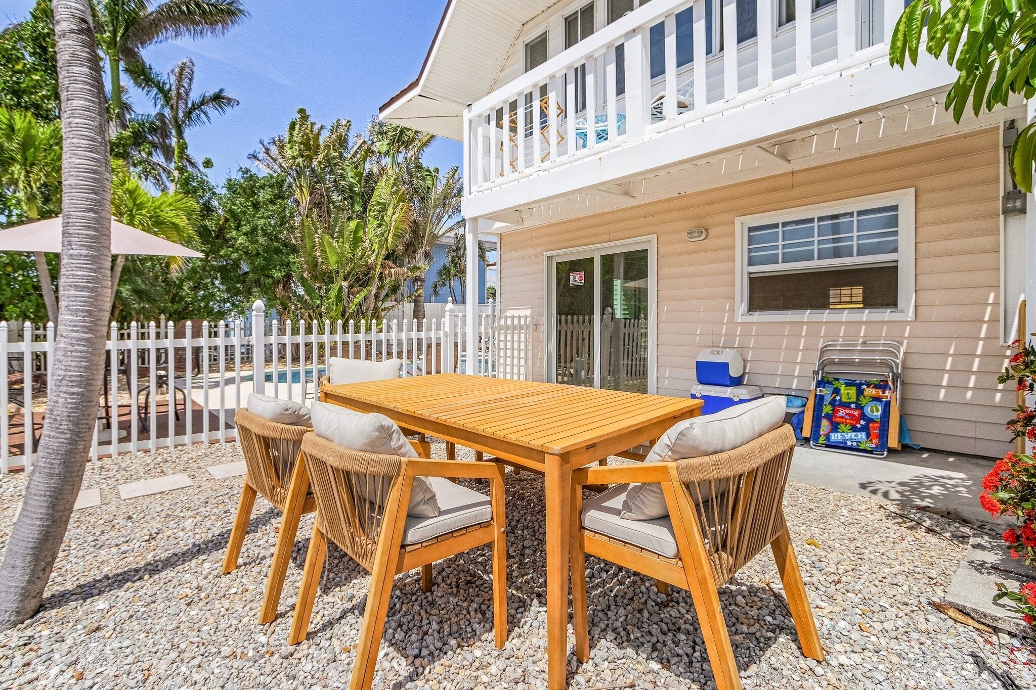 A wooden table with four chairs, a white fence, and a pool in the background.