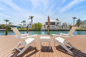 A wooden deck with two white lounge chairs and a small table, overlooking a body of water and a row of houses. - 21591/3 Waterfront Duplex With Pool And Spa - Manor 4 Bedroom Home (Fort Myers Beach)