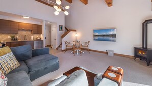 A modern living room with a grey sofa, a coffee table, and a fireplace. There is a kitchen area with wooden cabinets and a dining area with a table and chairs. - Timber Creek 309 1 Bedroom Condo (Truckee)