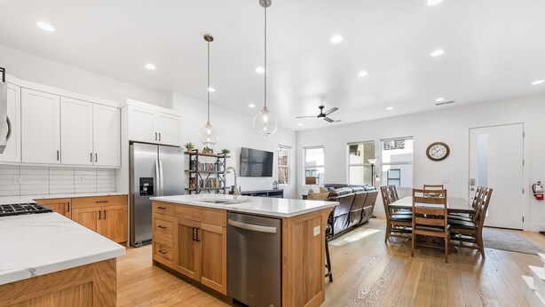 Una cocina moderna con armarios blancos, un refrigerador de acero inoxidable, piso de madera y una zona de comedor con una mesa y sillas de madera.