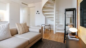 A modern living room with a sofa, a chair, a spiral staircase, and a side table with books and a lamp. - Feel Porto Cl Rigos Charm Flat 4 2 (Porto)