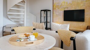 A modern living room with a spiral staircase, a flat-screen TV mounted on the wall, and a breakfast tray on a round table. - Feel Porto Cl Rigos Charm Flat 4 2 (Porto)