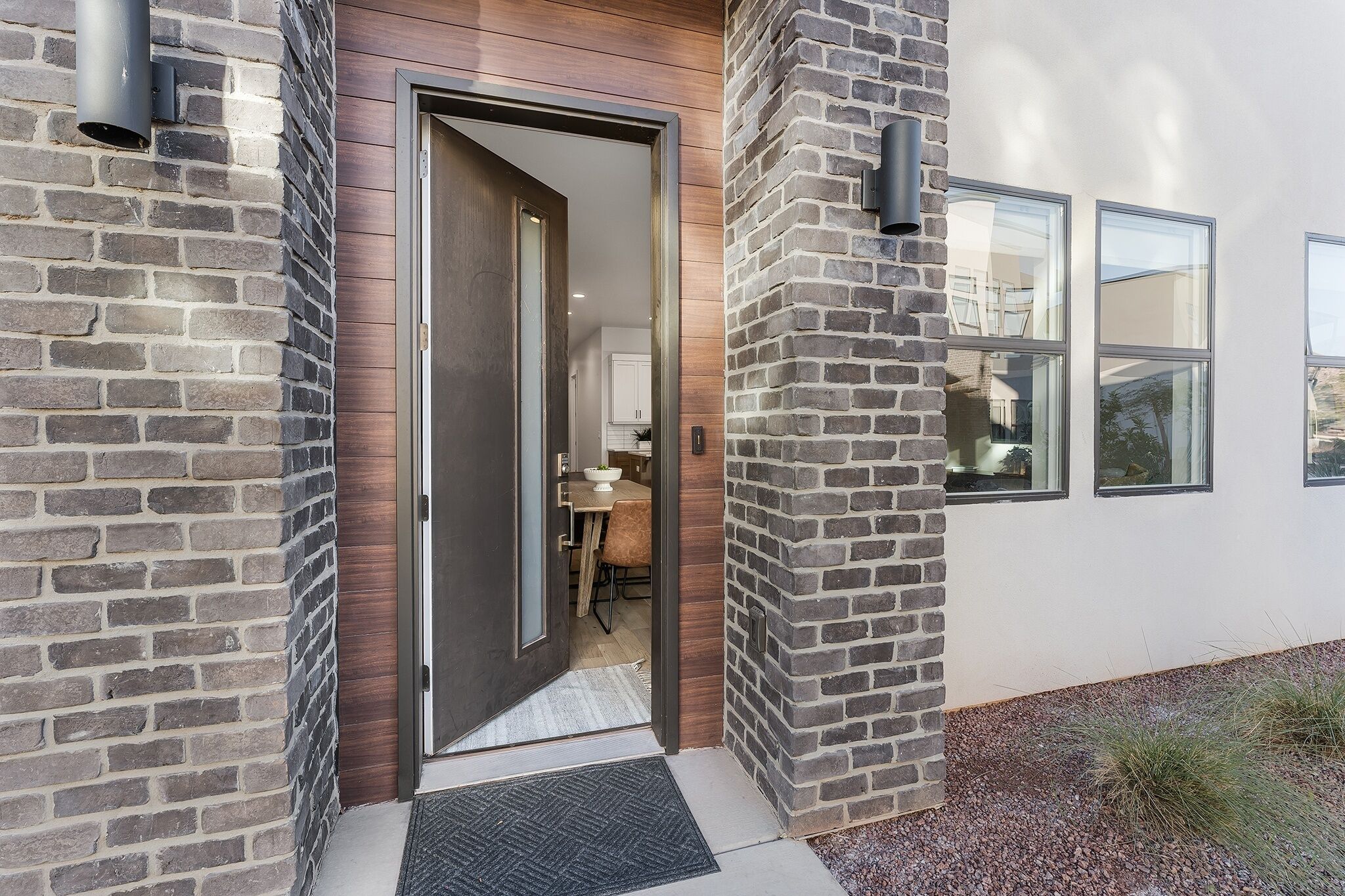 A modern house entrance with a wooden door, brick walls, and a small garden area.