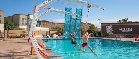 Una piscina con tobogán y pared de escalar, rodeada de sillones de descanso y un edificio que dice 'el CLUB'.