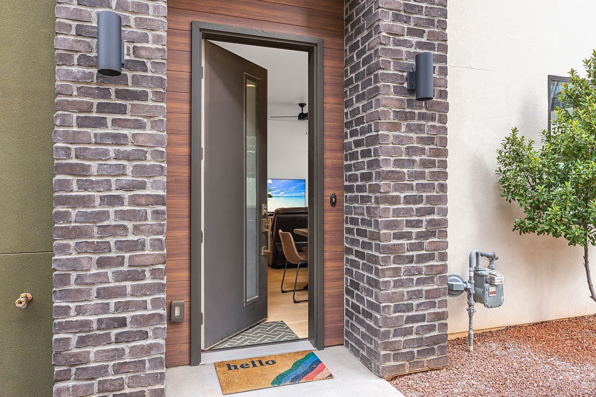 Una entrada moderna de edificio con fachada de ladrillo, una puerta de madera y un espacio de oficina visible en el interior.