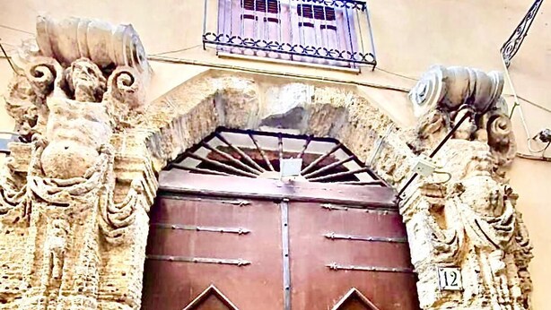 Una puerta doble grande y ornamentada con intrincados grabados y un portón de metal, incrustada en una construcción de piedra.