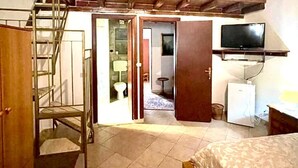 Un dormitorio con cama tipo altillo, televisor, refrigerador y baño visible a través de una puerta abierta.