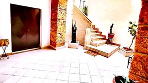 Amplio espacio interior con piso de baldosas, una escalera que sube a un nivel superior y varias plantas en macetas.