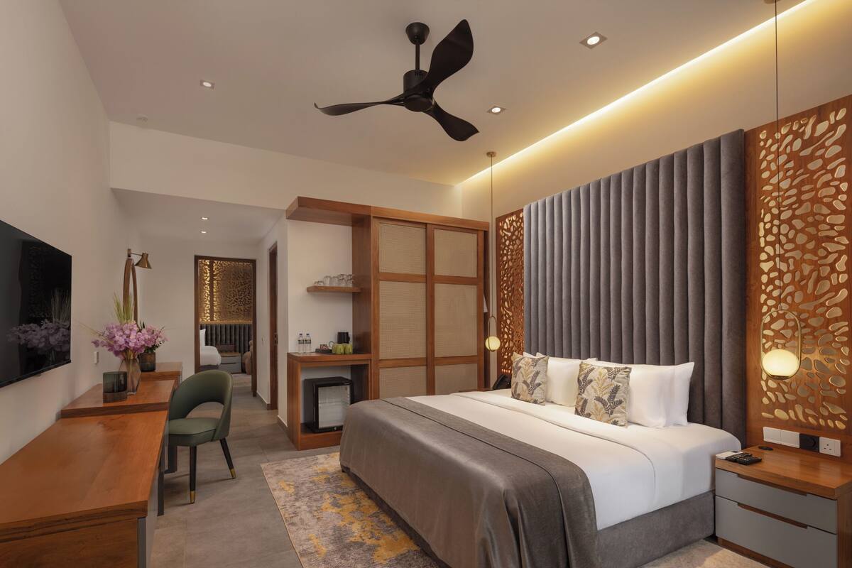 A modern hotel room with a bed, desk, chair, and a ceiling fan.