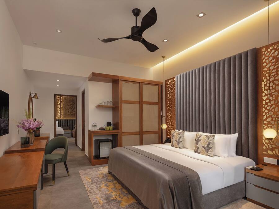 A modern hotel room with a bed, desk, chair, and a ceiling fan.