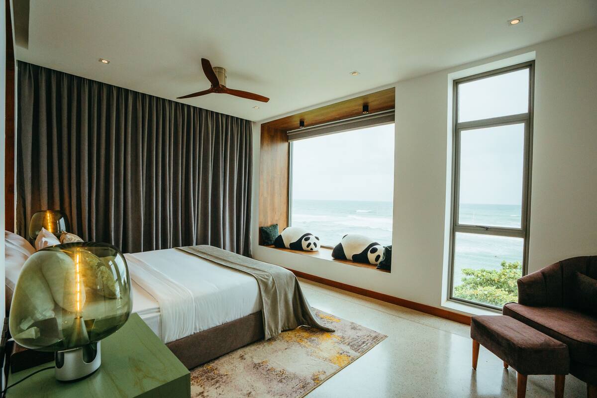 A bedroom with a large bed, a view of the ocean, a panda-themed window seat, and a ceiling fan.